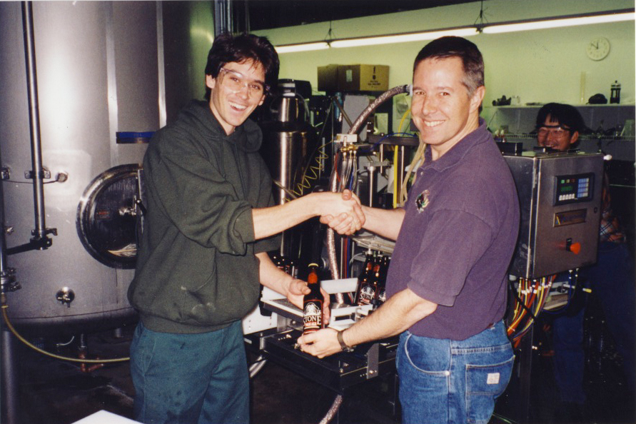 Lee Chase and Steve Wagner showcasing our first ever 12 oz. bottle with Stone Brewer, Toshi Ishii looking on. Note that the "Maheen" bottling machine in the background is roughly the size of the three of them.