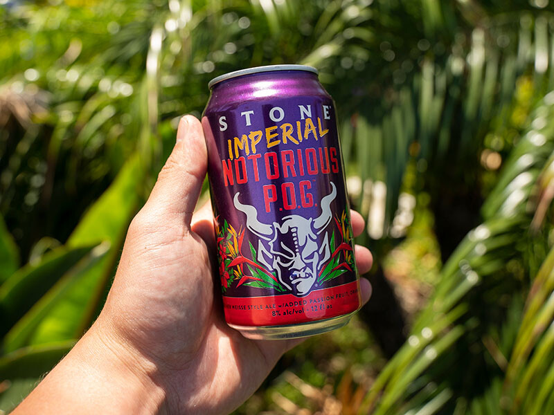 hand holding a can of Stone Imperial Notorious P.O.G. in front of tropical leaves reminiscent of hawaii