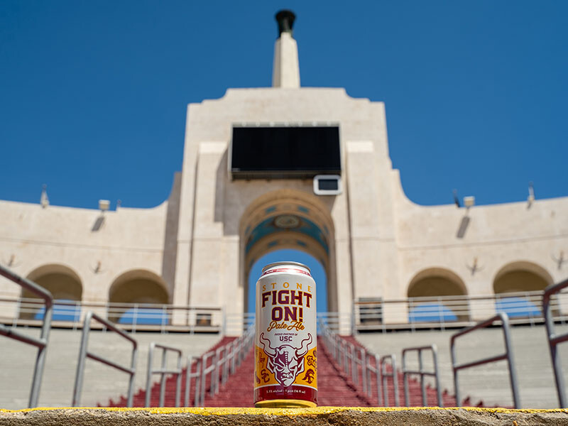 a can of the Stone Fight On Pale Ale beer in the USC football stadium in front of the iconic entrance