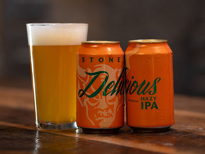 glass and two cans of stone delicious hazy ipa