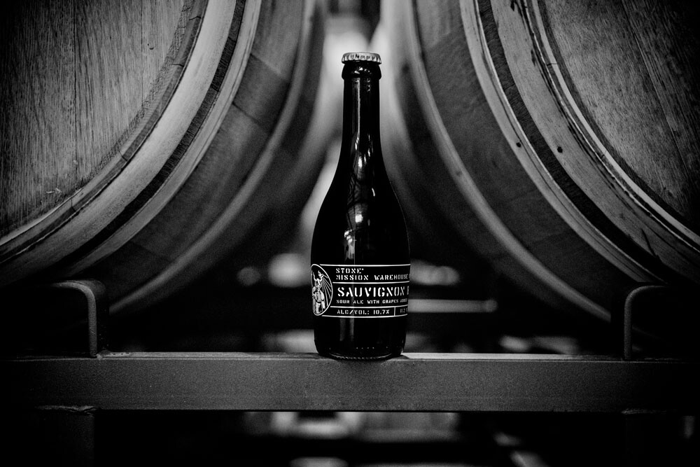 Stone Mission Warehouse Sour - Sauvignon Blanc bottle in front of barrels