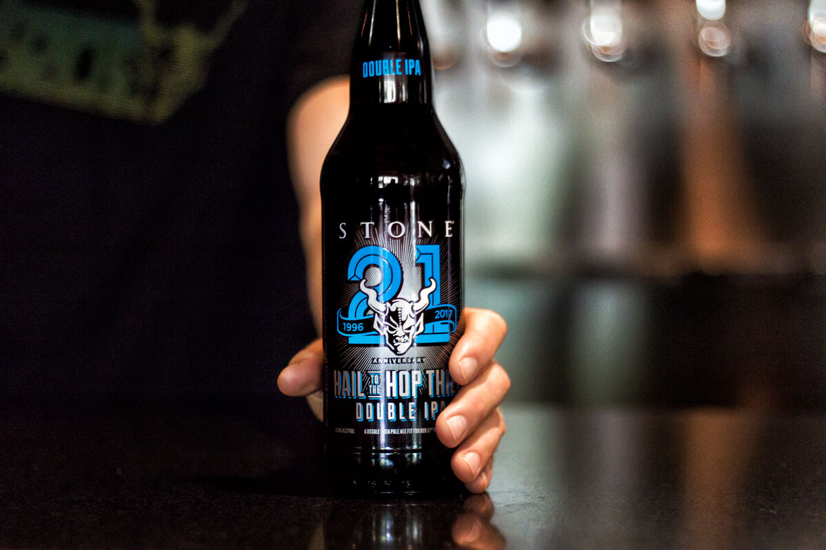 Hand holding a bottle of Stone 21st Anniversary Hail to the Hop Thief Double IPA on a bar