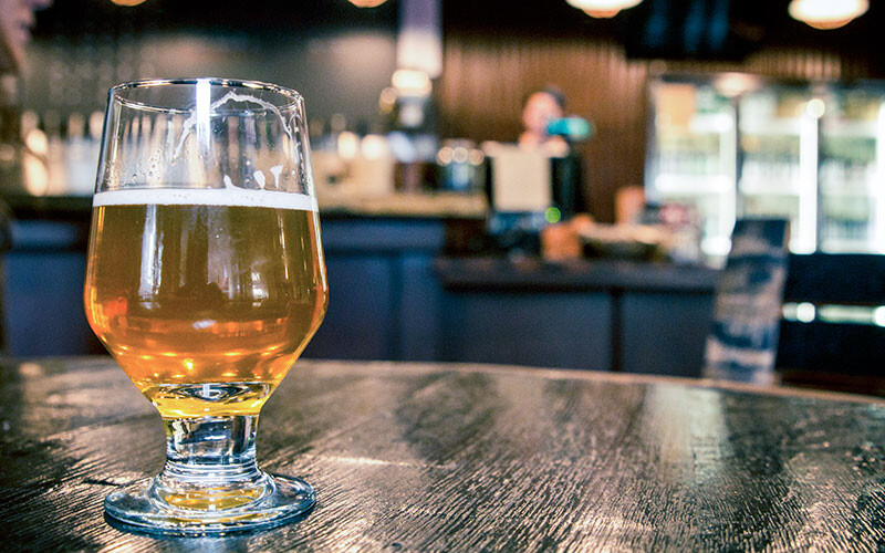 a glass of beer on a table in front of the bar of stone brewing tap room kettner in downtown little italy san diego